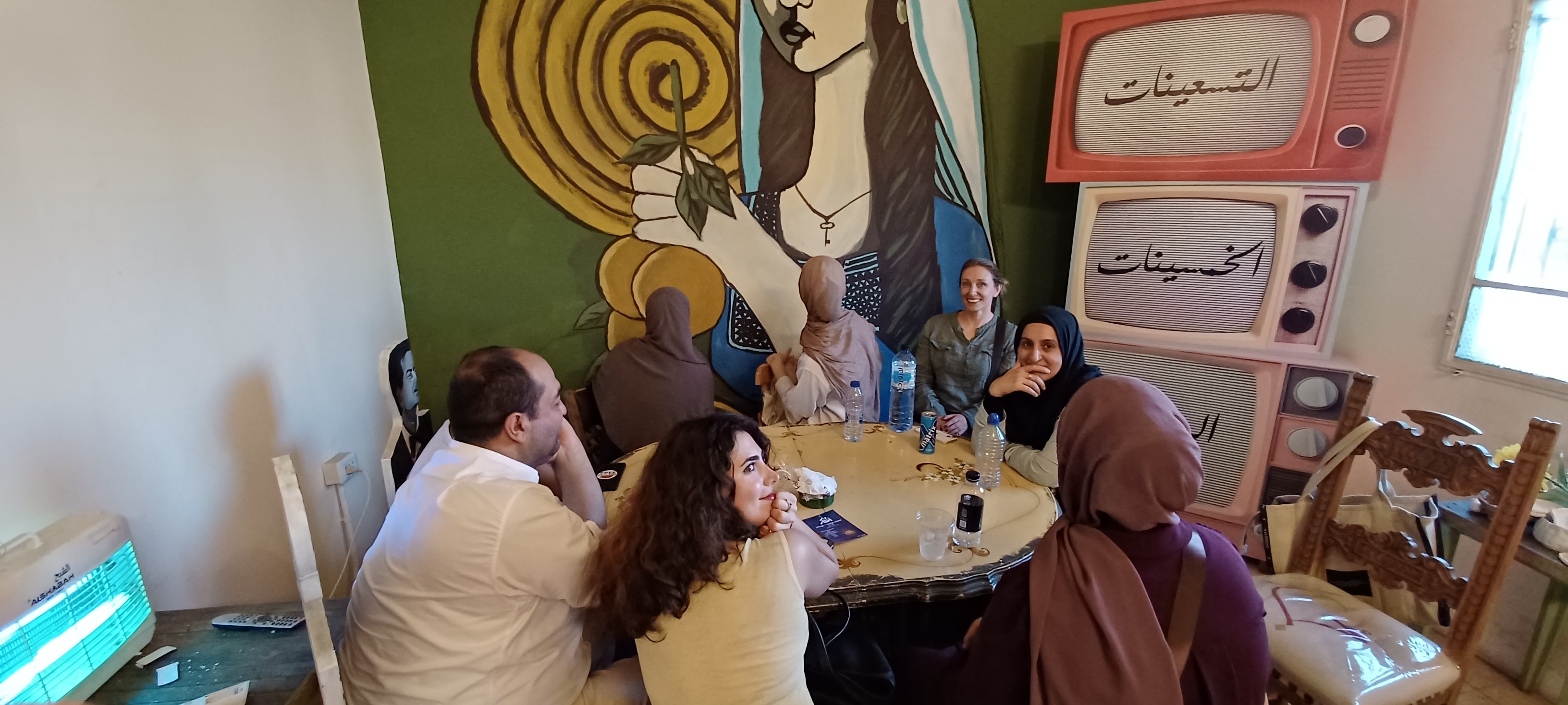 جلسة تبادل لغوي حول الطاولة مع لوحات جدارية في مساحة جدل